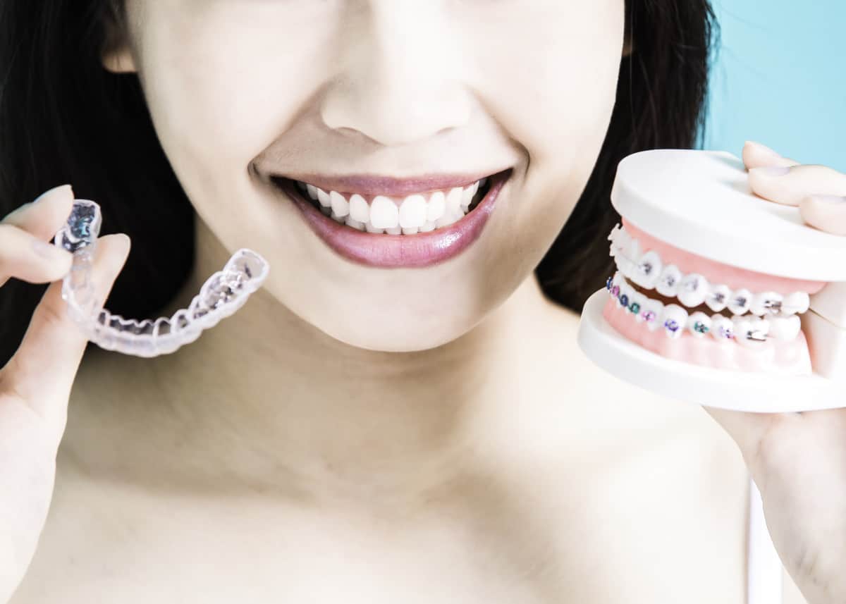 a woman smiling holding up a dental model with braces and a clear aligner