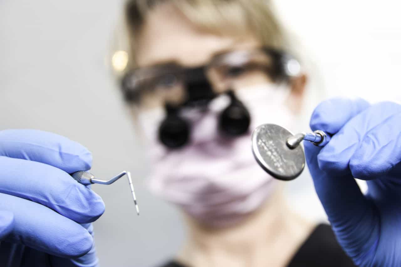 Dental Hygienist holding a periodontal probe and mirror looking over patient 