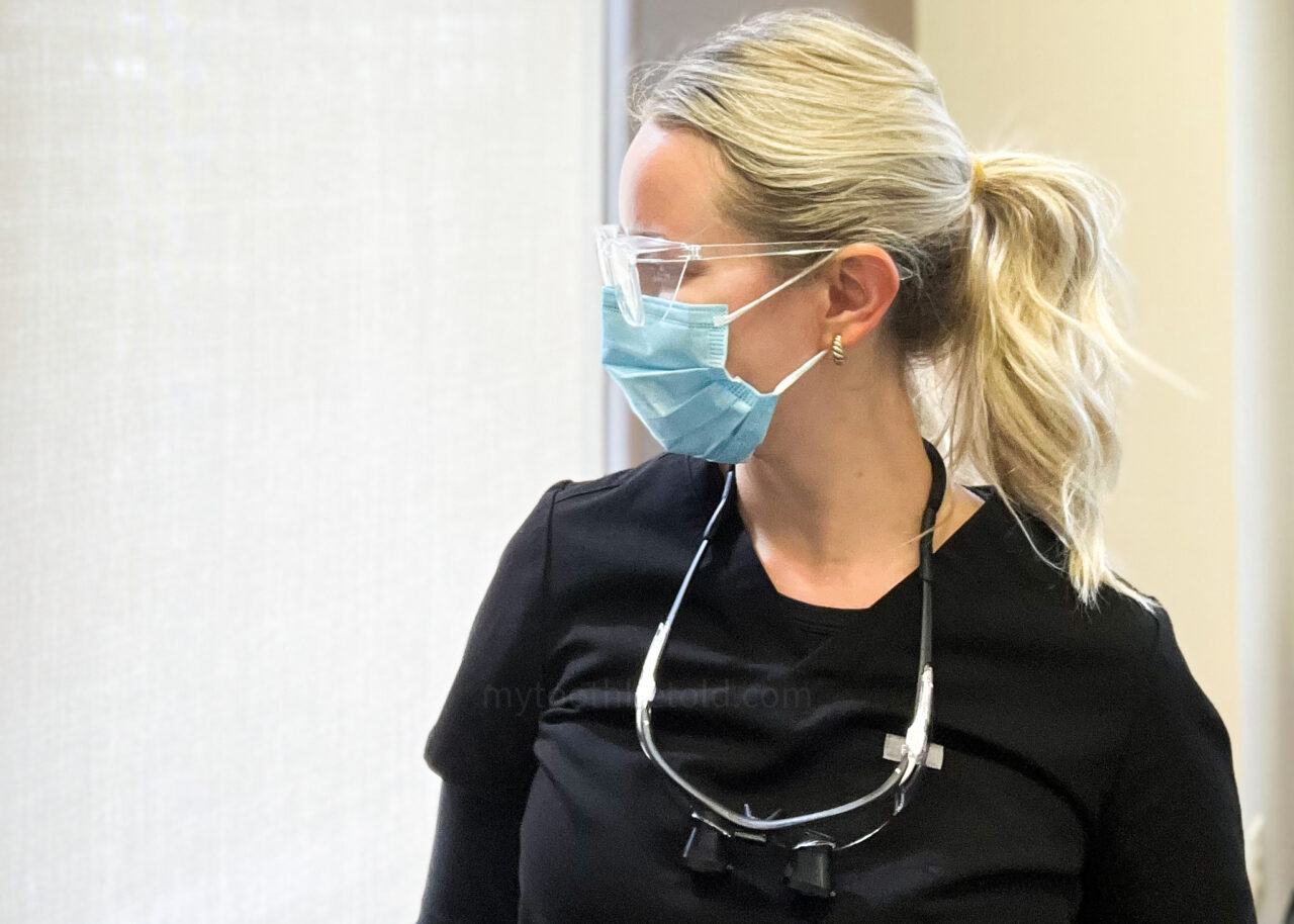 Holly Verran RDH is wearing black scrubs, a blue mask and safety glasses.